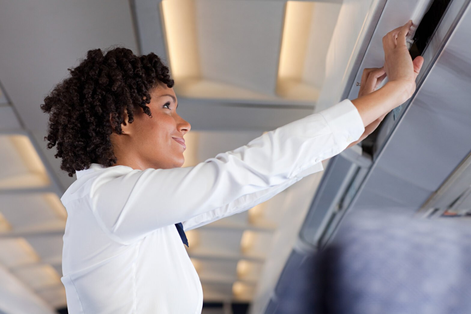 A passenger places a carry-on bag in an airplane overhead compartment during a flight.