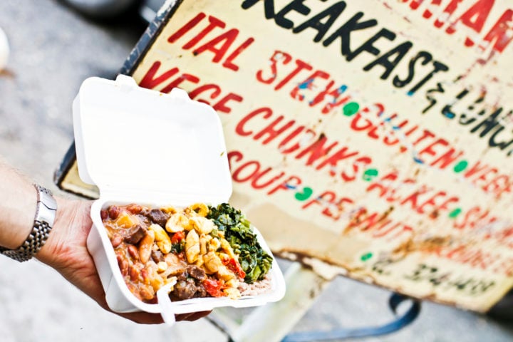 Kingston, Jamaica - January 19, 2012: Hand holding a take away plate of vegetarian rasta food (ital food) in front of the restaurant sign in downtown market area.