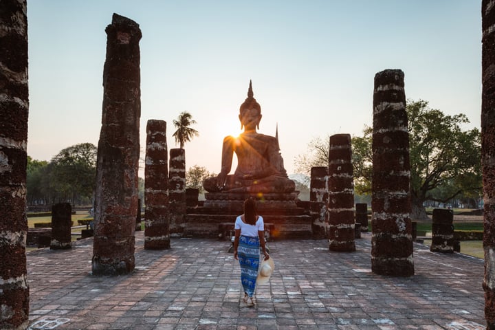 woman walking toward statue in Thailand - most expensive destinations to fly to this summer