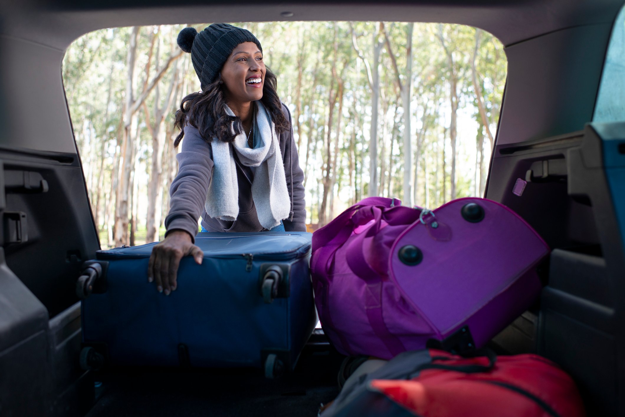 Happy woman taking a road trip break, taking out a bag from the car trunk.