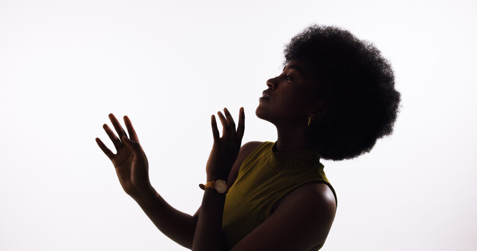 Silhouette of a person in profile against a bright white background, with a natural afro hairstyle. They wear a sleeveless olive-green top and a wristwatch, lifting both hands gently toward their face as if in a moment of reflection or dance, light outlining their facial features and arms.