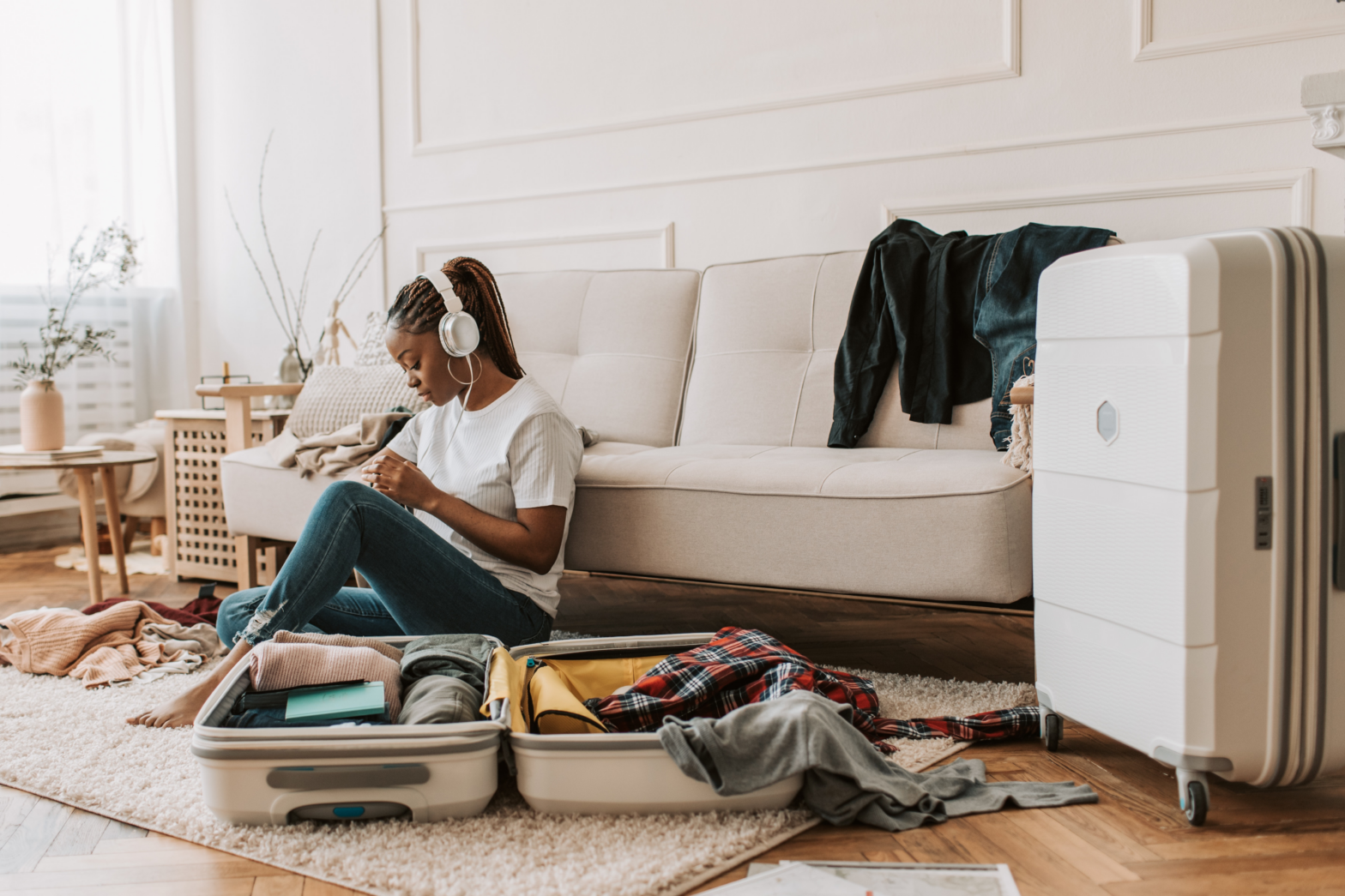 A young Black woman unpacks her luggage while listening to music during a fly and swap vacation.