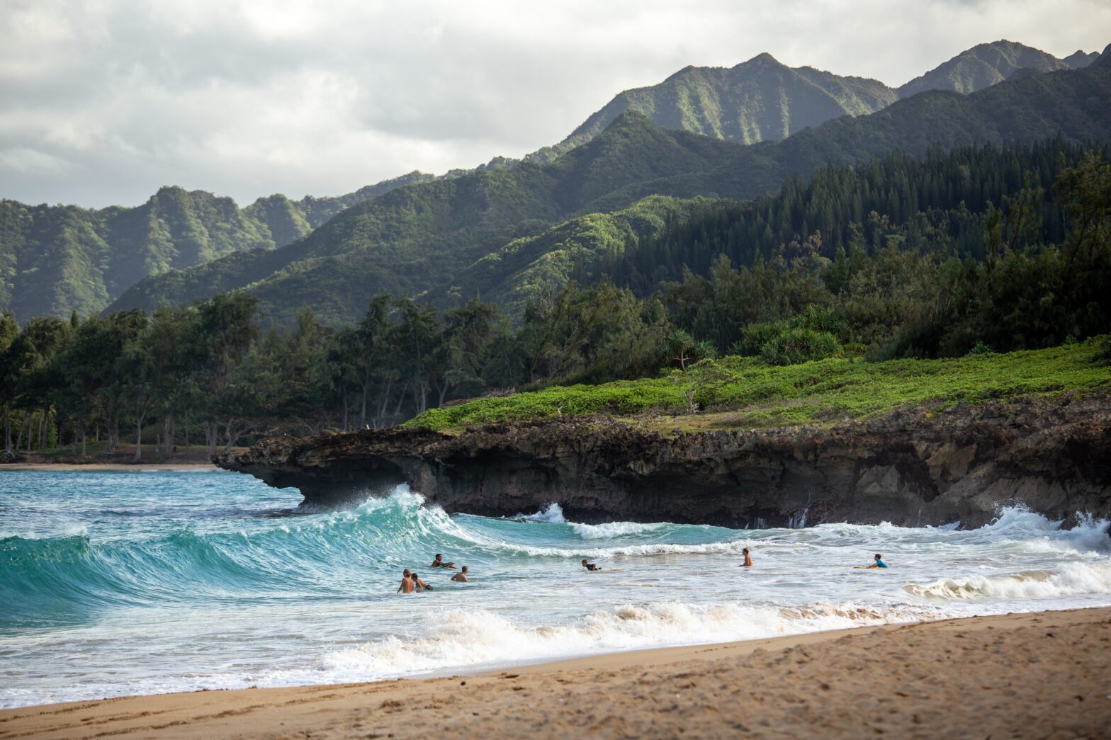Learn more about China Walls and the dangers of jumping its jagged Hawaiian cliffs. pictured: black volcanic cliffs in Hawaii with green lush mountains in the background