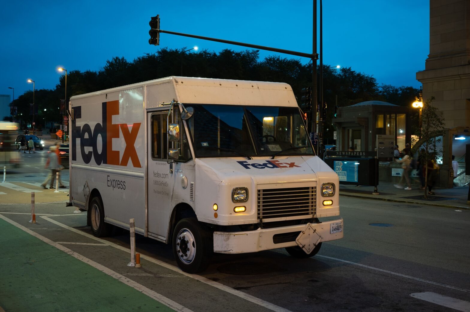 A FedEx delivery truck parked on a street in a city at night illuminated by the street lights