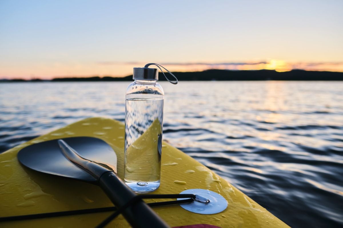 water bottle standing on a paddle board at sea during sunset