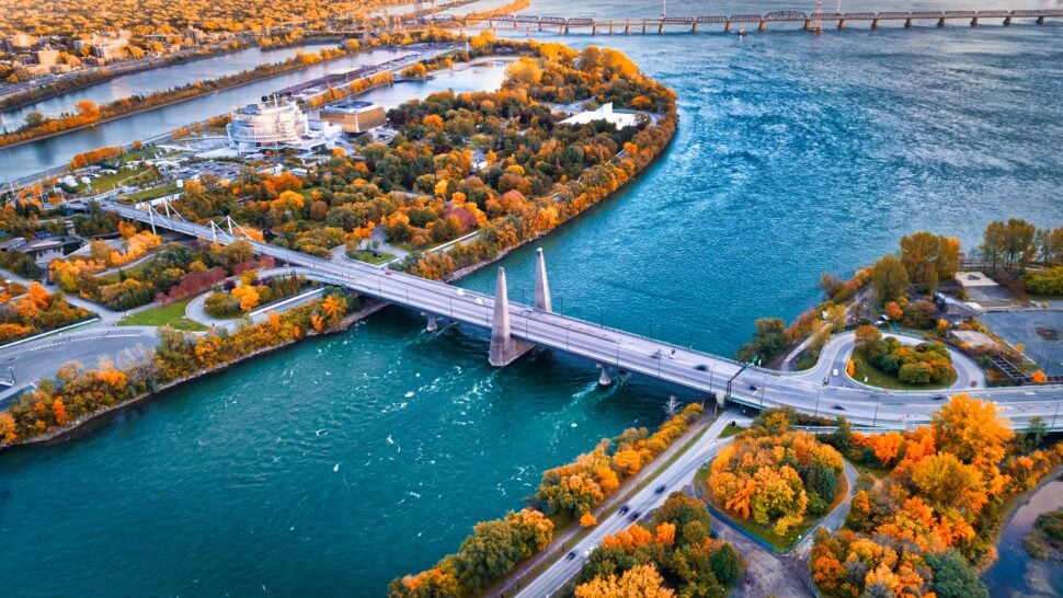 Aerial view of Montreal in autumn, with colorful fall foliage surrounding waterways, bridges, roads, and city buildings.