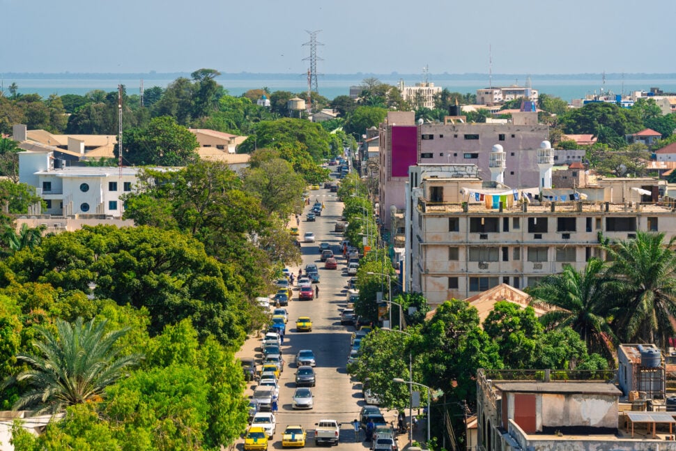 Banjul, Gambia. Elevated view down Independence Drive, a main street of the capital city, lined with buildings and green trees.