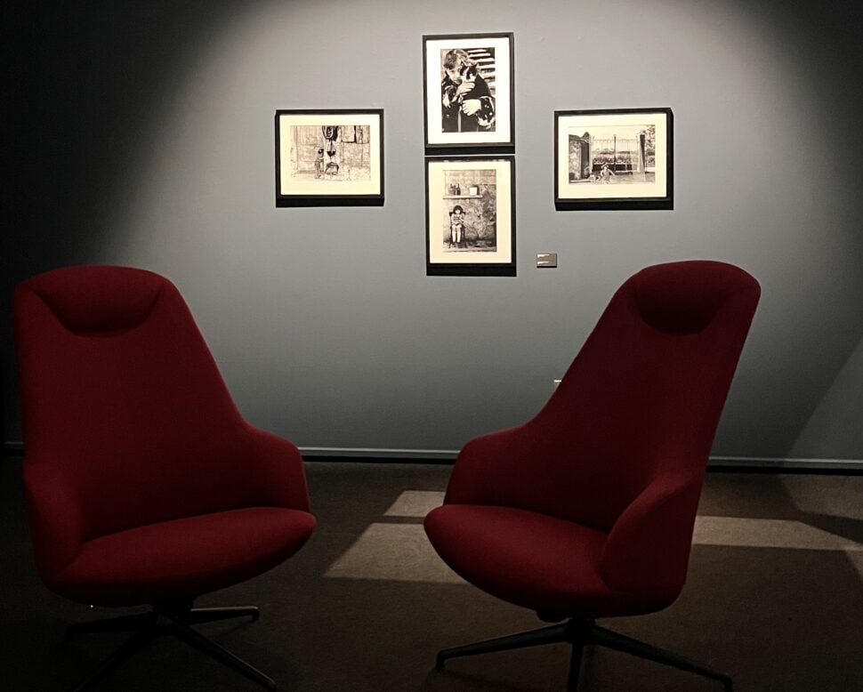 Two red chairs beneath a spotlighted display of Carla Cerati photographs.