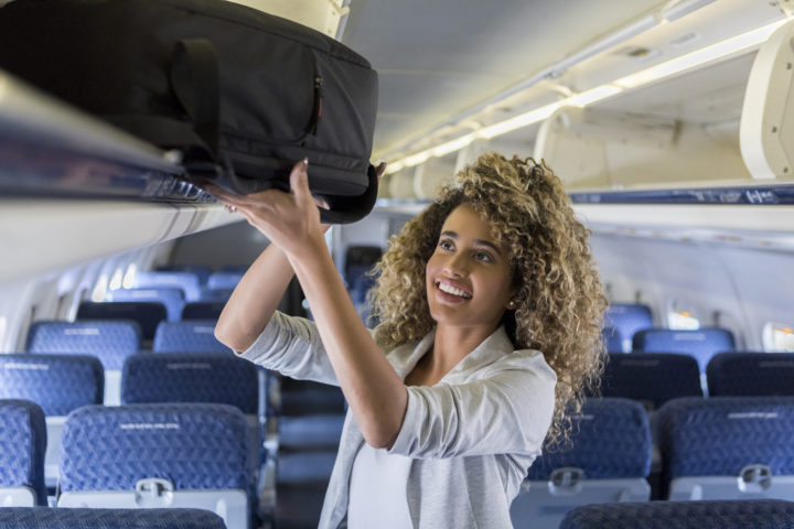 Woman putting bag in overhead compartment. why you should place your luggage in the bathtub