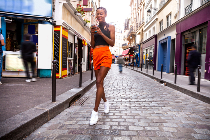 Young black women walking in Paris in the city center talking and texting on the phone and commuting using one of public city bikes.