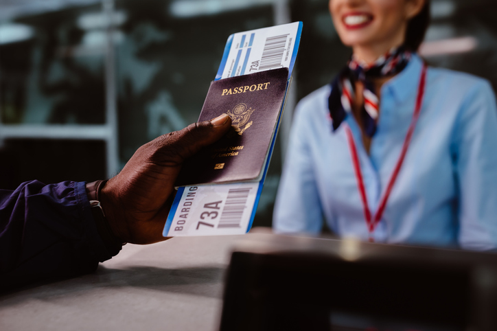 African American man holding boarding pass and passport at airline check-in desk at international airport