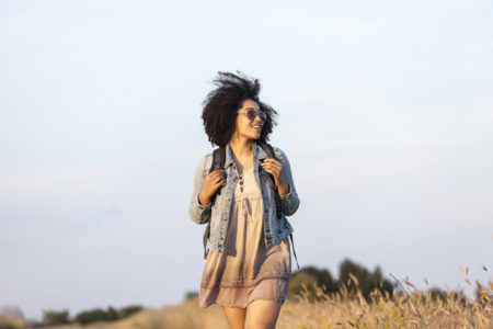 Carefree african woman walking on empty country road, enjoying the sun.