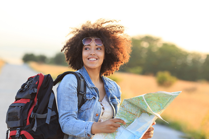 Black woman holding a map outdoors with backpack