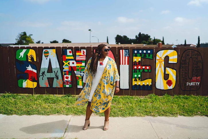 Pictured: a black woman standing in front of a sign that says San Diego on a sunny day.