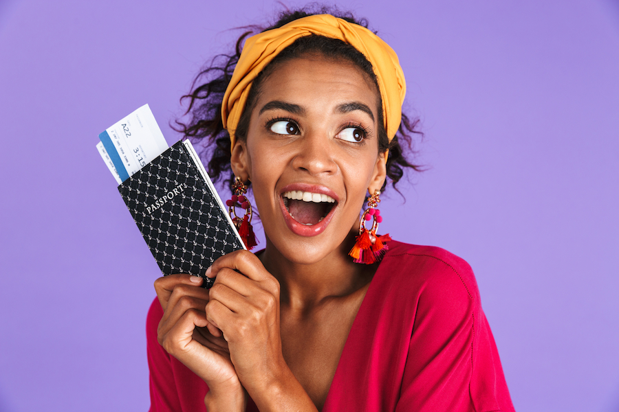 Playful African woman in dress holding passport with tickets