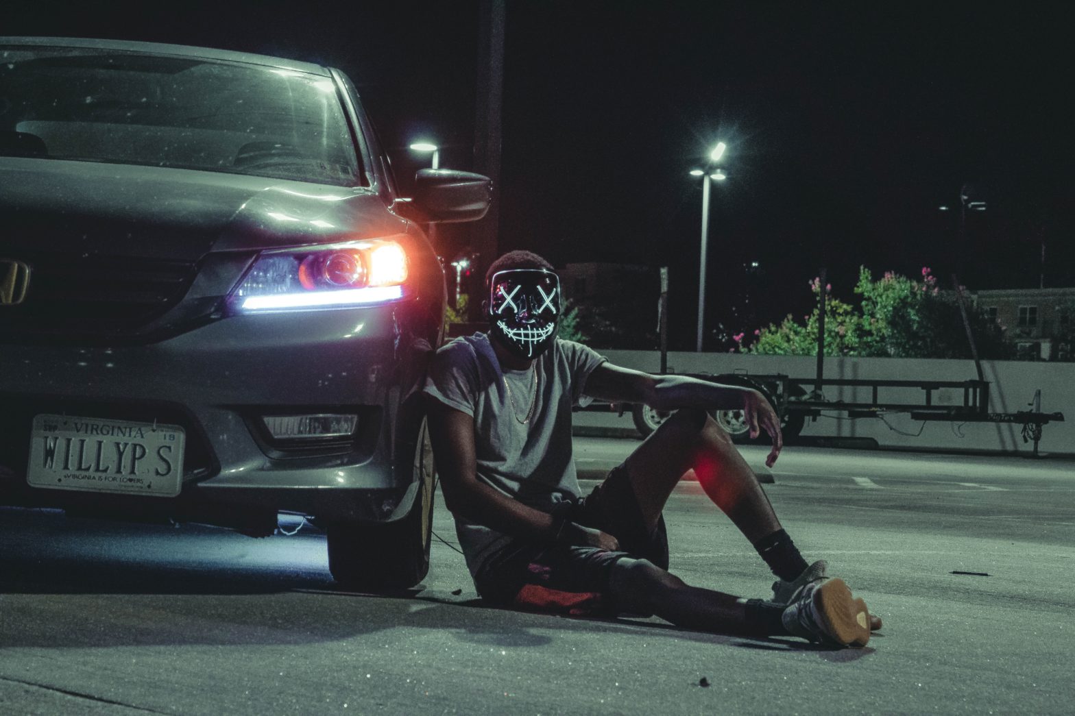 Illinois Becomes The First State To Pass "The Purge" Law. Pictured: A person with a black mask featuring a creepy facial expression sitting against a car at night.