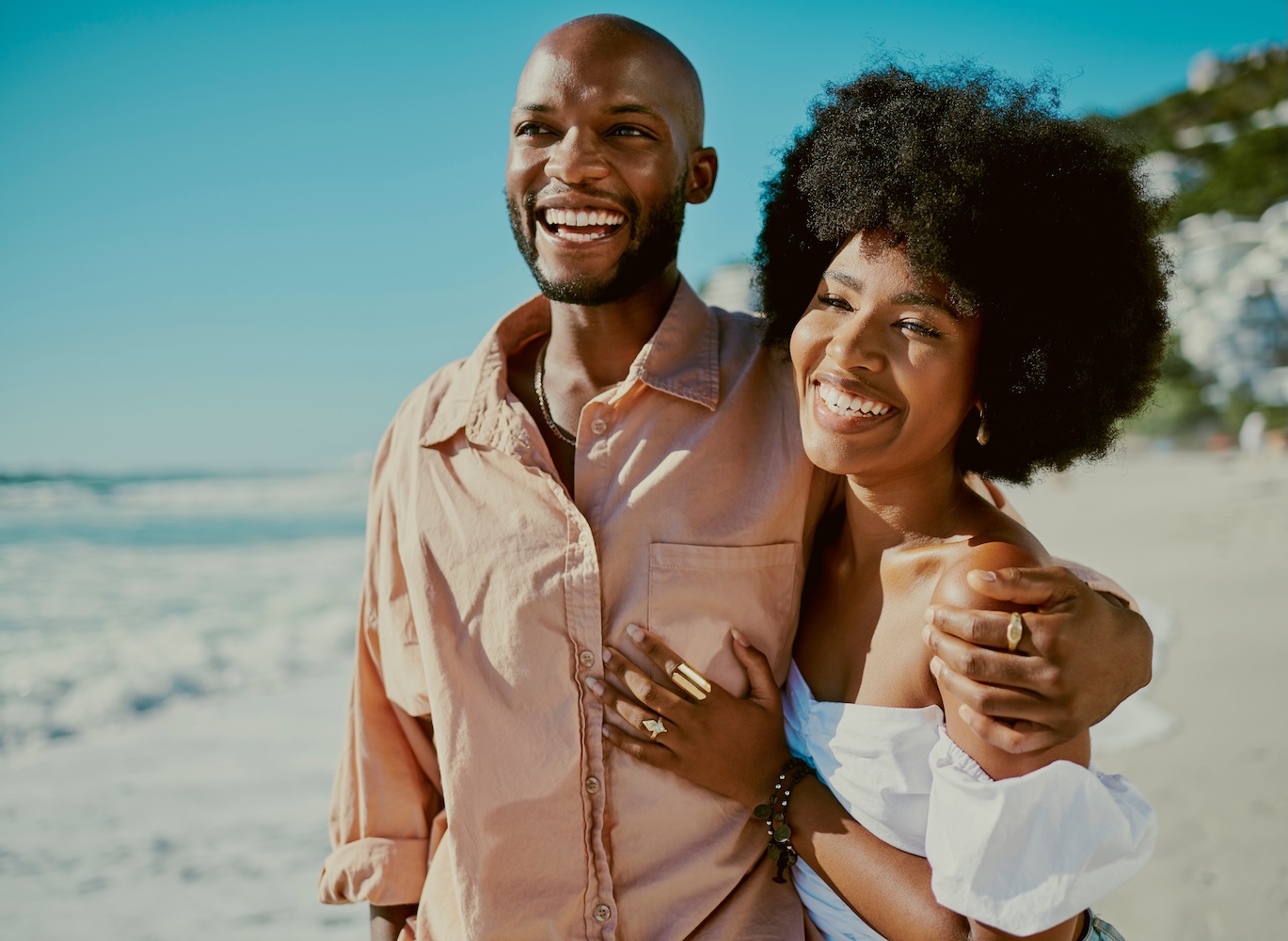 Young happy Black couple smiling, bonding and walking on beach together during summer.