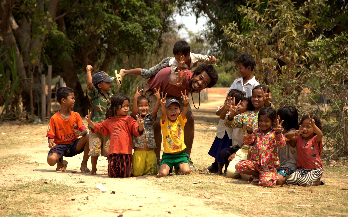 Grammy Award-Winning Artist evrYwhr in Cambodia smiling with group of children on Destination evrYwhr, a KevOnStage Studios production