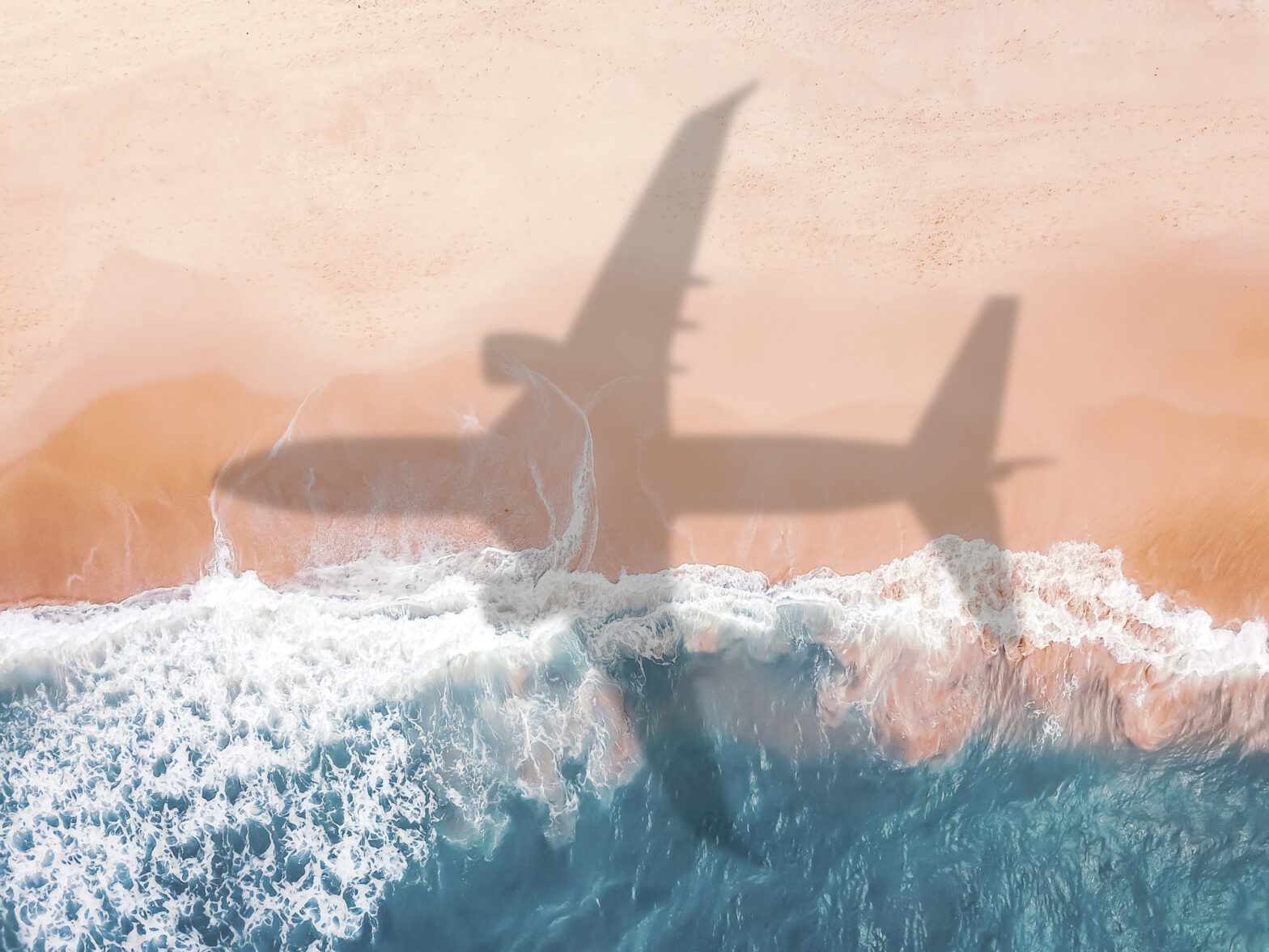 Aerial view of an airplane shadow over a sandy beach.