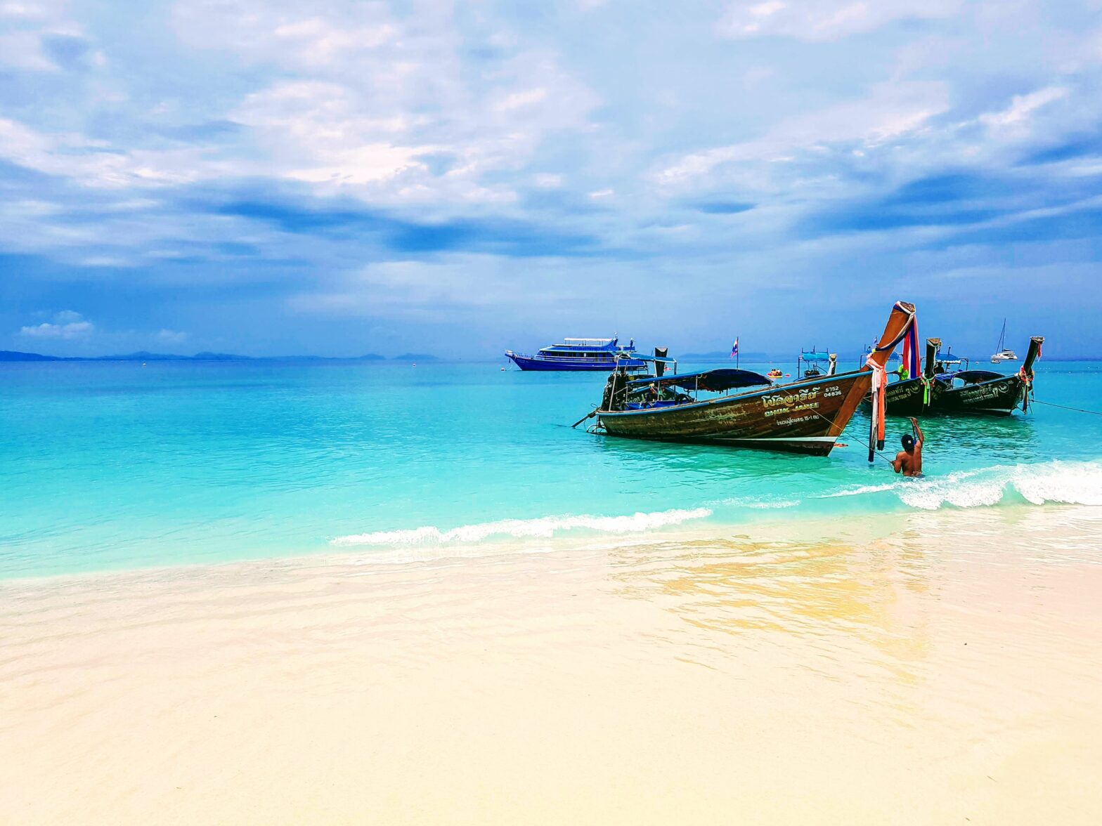 traditional wooden boat in the clear turquoise blue waters on the beach shoreline of Phuket, Thailand