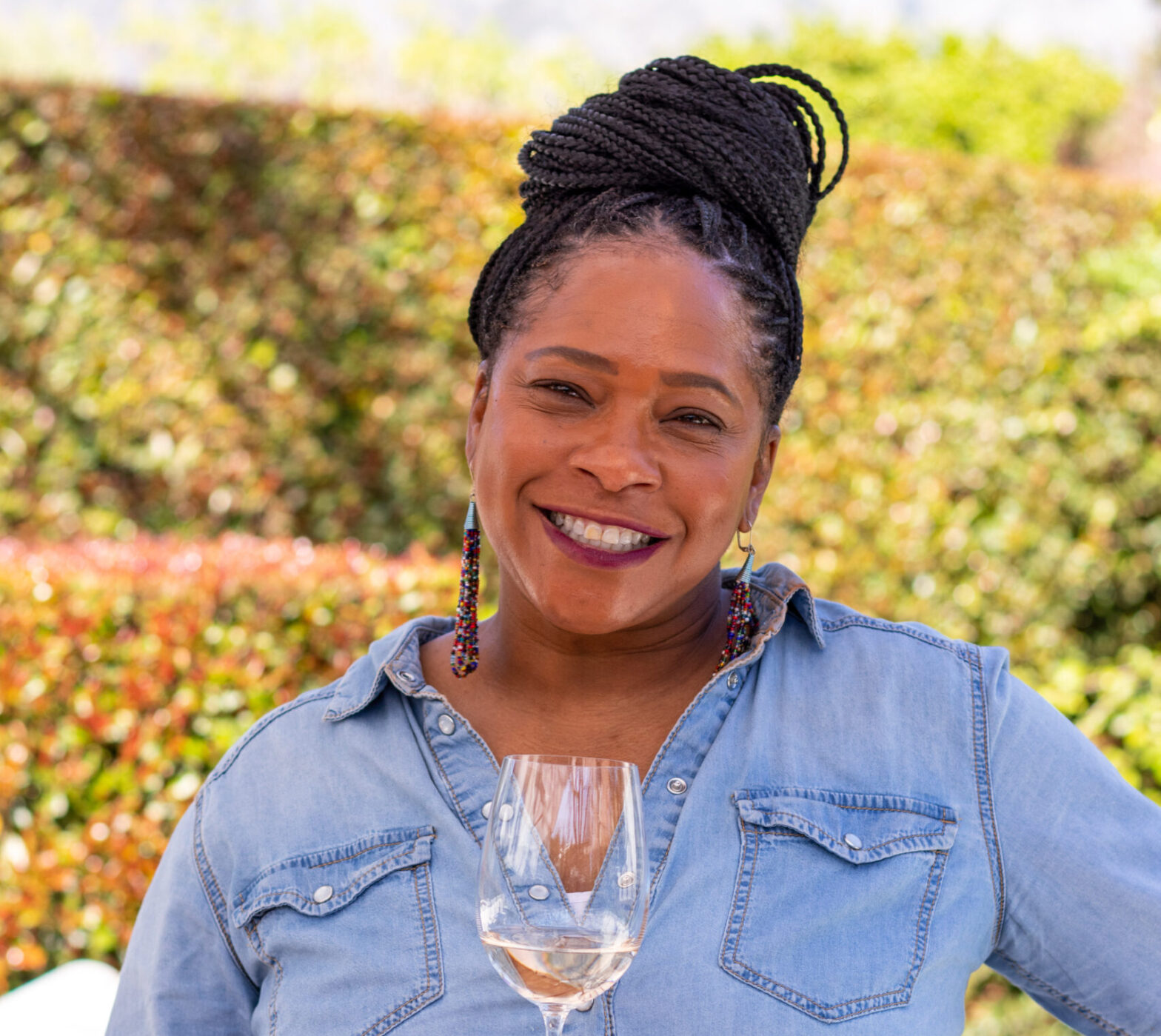 Black woman wearing light denim with dark brown skirt and holding white wine glass