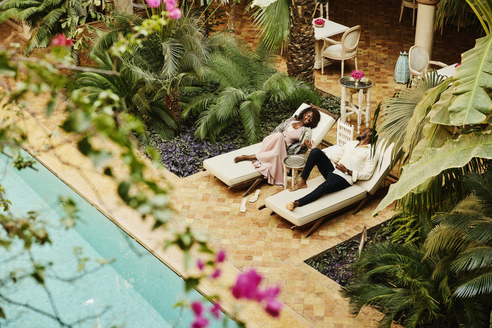 Wide high angle shot of couple relaxing in lounge chairs by pool in courtyard of luxury hotel while on vacation.