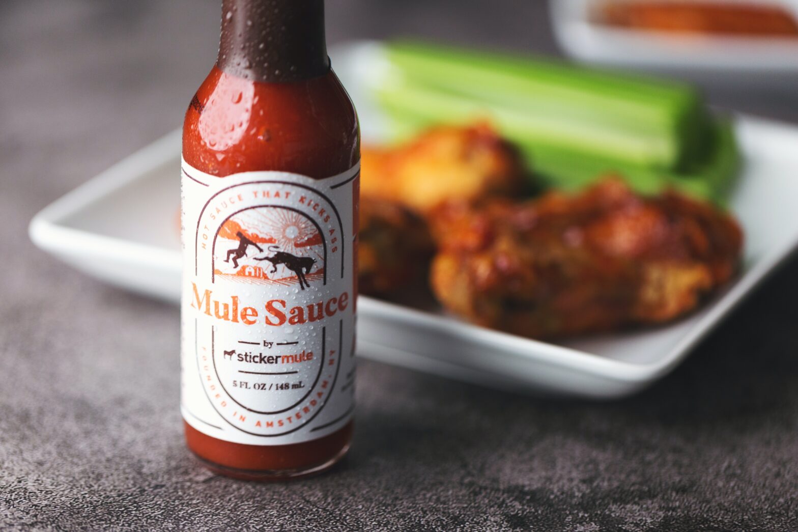 bottle of hot sauce and chicken wings on a plate