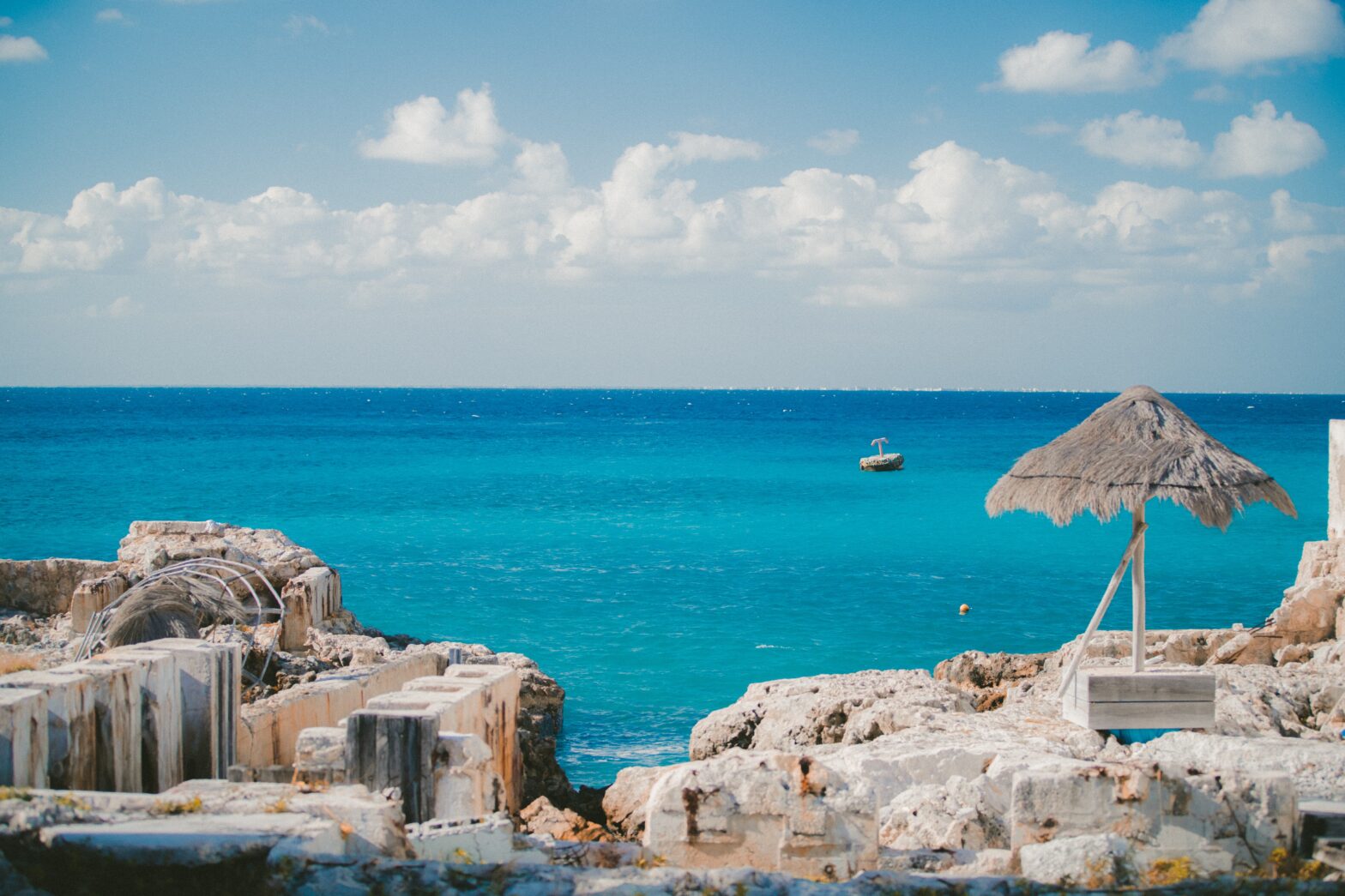 Cozumel is a Mexican-Carribbean island that offers travelers a unique getaway. Learn more about what makes the island safe. pictured: A tranquil Cozumel shore with a boat off in the distance on a sunny day