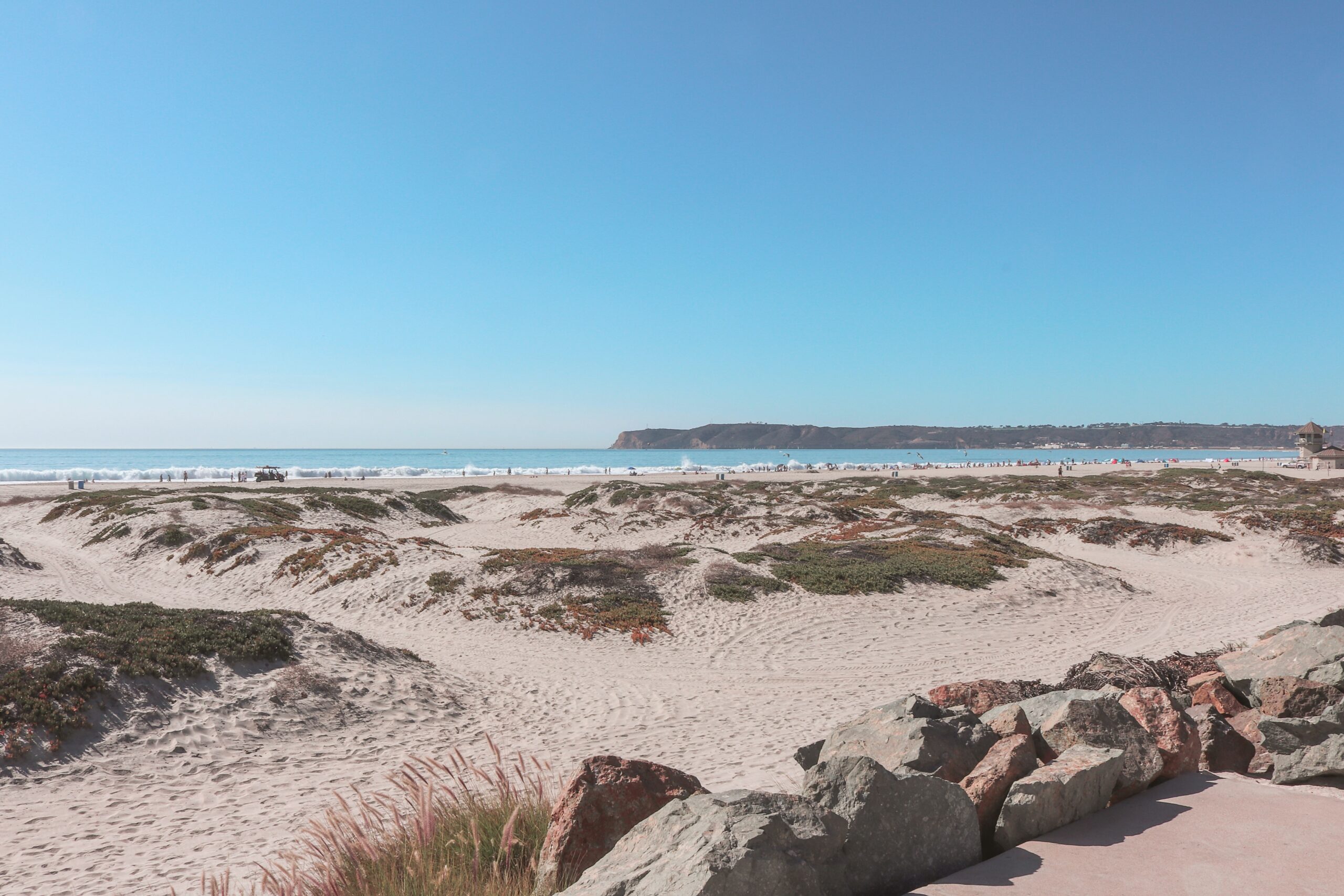 NAS North Island in San Diego is a beautiful film location from the film Top Gun. 
pictured: The sandy coast of NAS North Island with visitors enjoying the California sun off in the distance