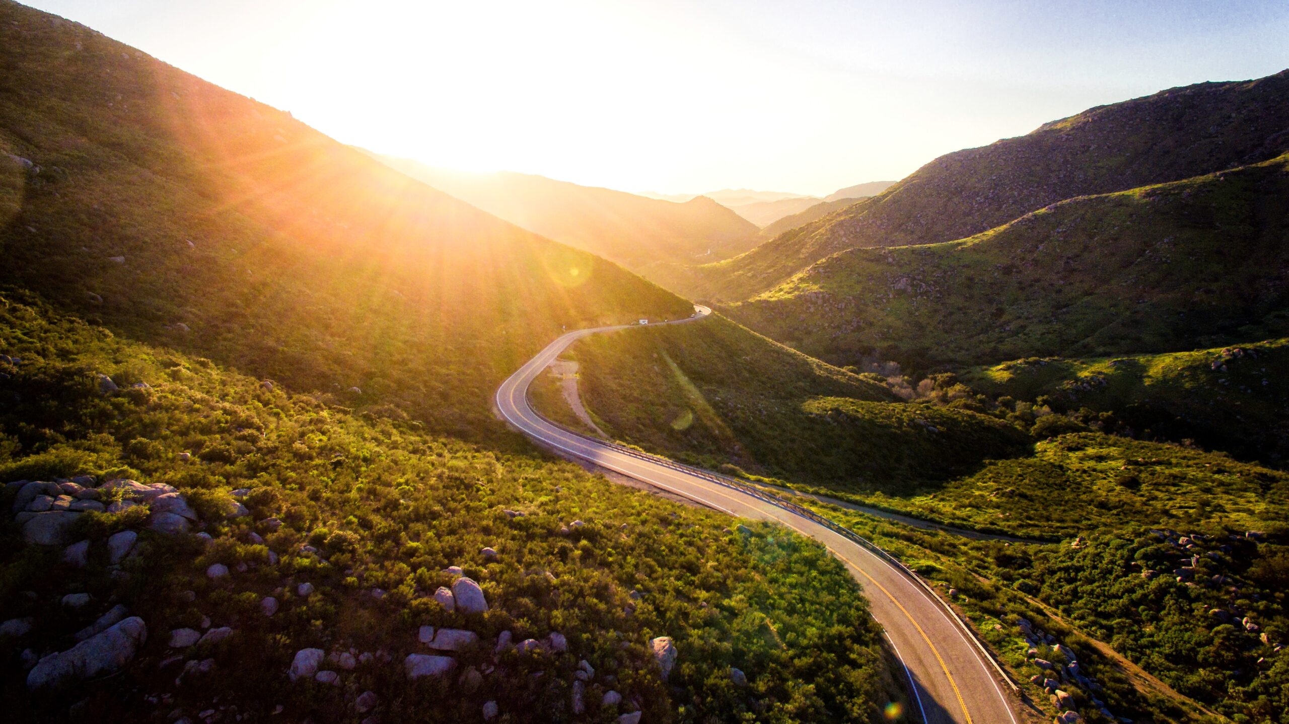 Check out the digital games that will make a road trip go as quick as ever. 
pictured: A green lush valley with rolling hills and a long winding road during a beautiful sunny day 