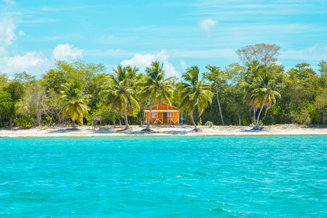 Here is a list of the safest Caribbean islands for those wanting to vacation there. Pictured: a wide shot of a small home sat on the beach across from the ocean in Dominican Republic.