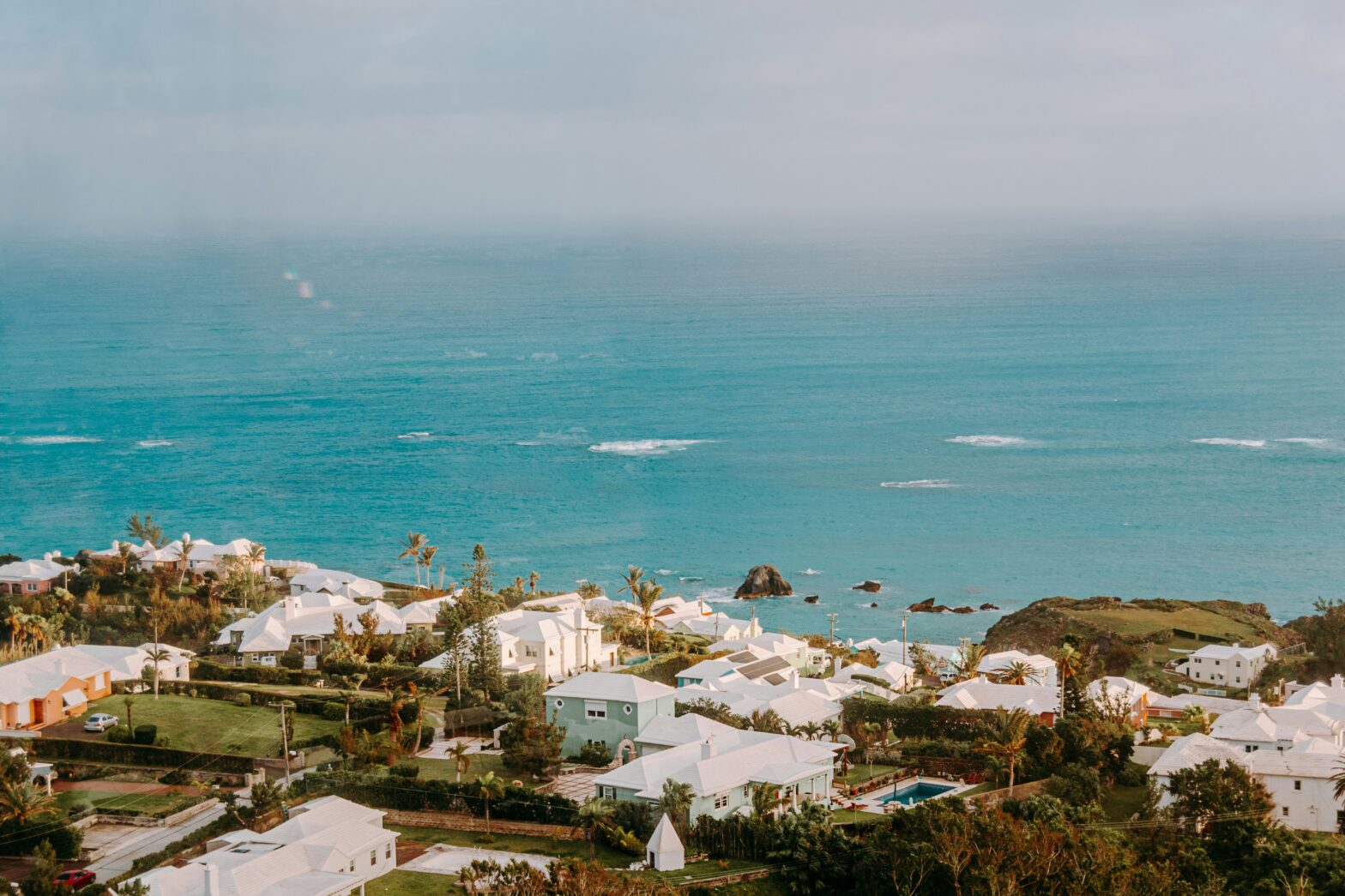 The turquoise beaches of Bermuda are perfect for a vacation. Learn more about if the Bermudian islands are safe. pictured: the shore of Bermuda with a small seaside town bordering it