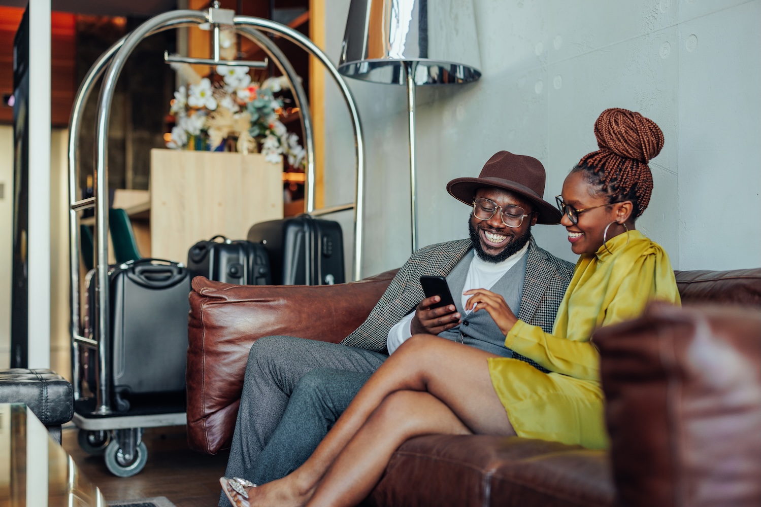 A smiling Black couple with luggage in a hotel lobby.