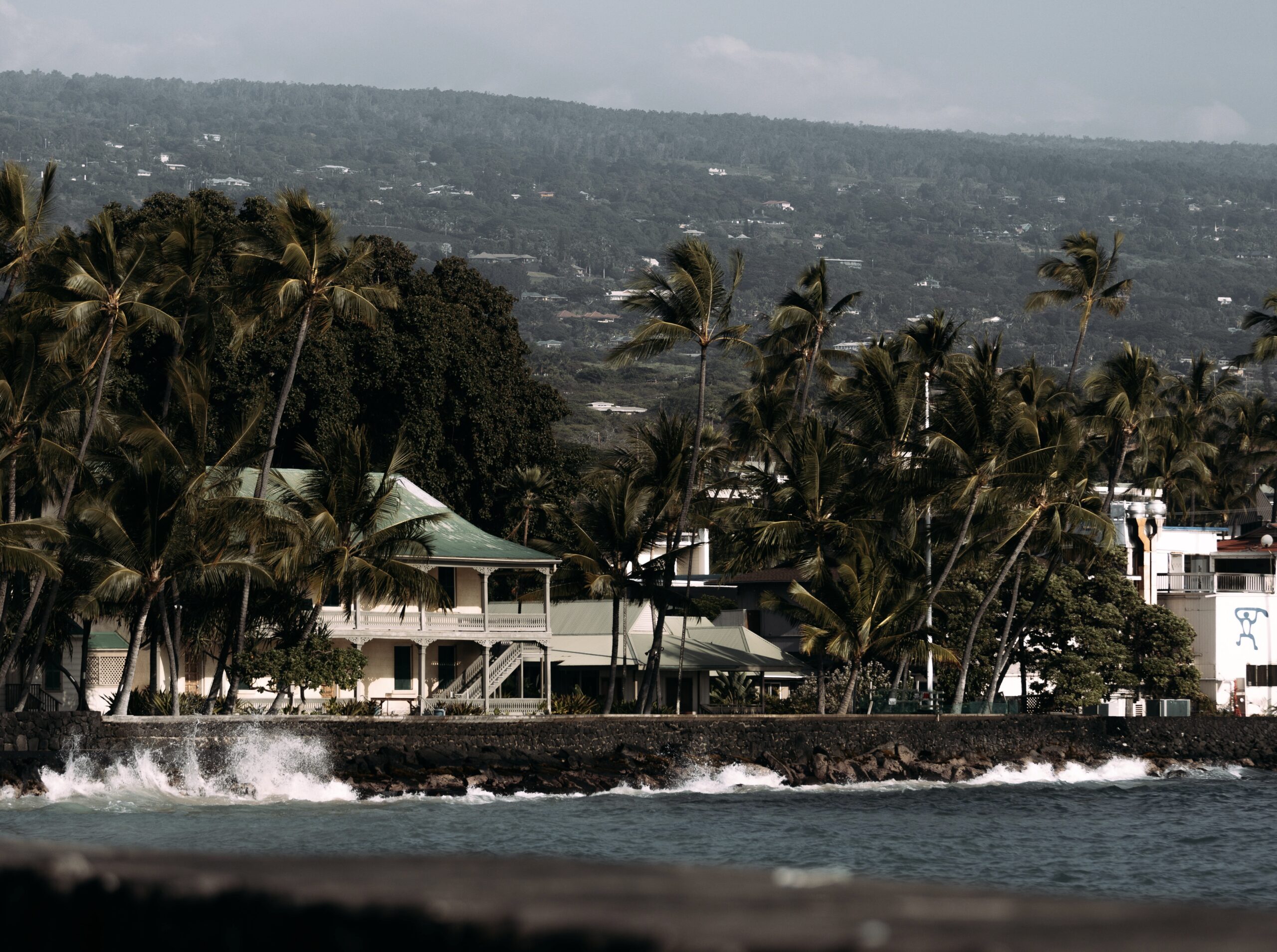 Magic Sands is a sunny cove in Hawaii that many tourists enjoy visiting. 
Pictured: the area and coast of Kona with green palm trees and hills 