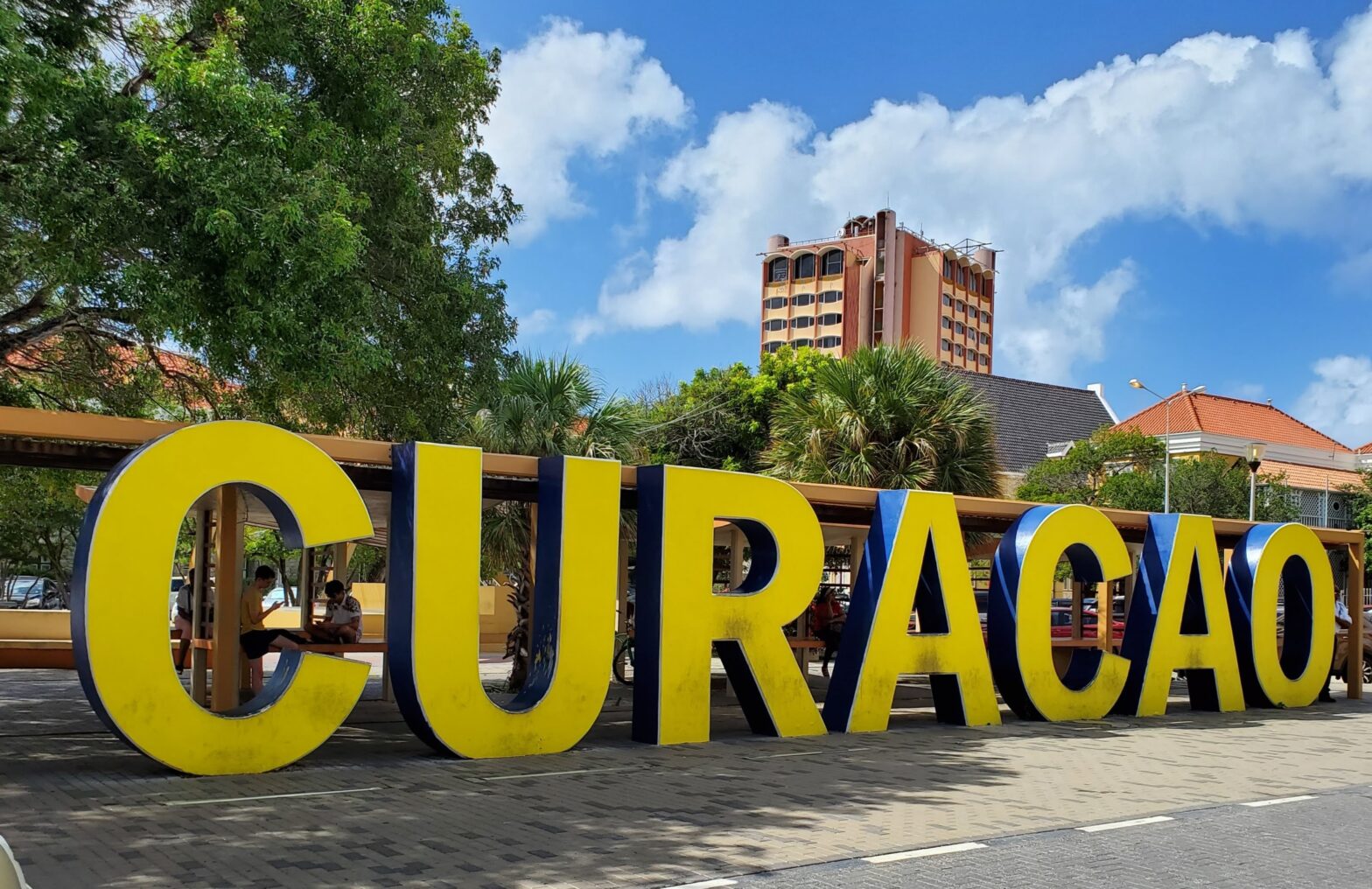 Curaçao is an ideal destination for a relaxed and safe island vacation. Check out the important information to know before visiting. pictured: a large yellow sign that says Curaçao in front of lush green trees and city buildings