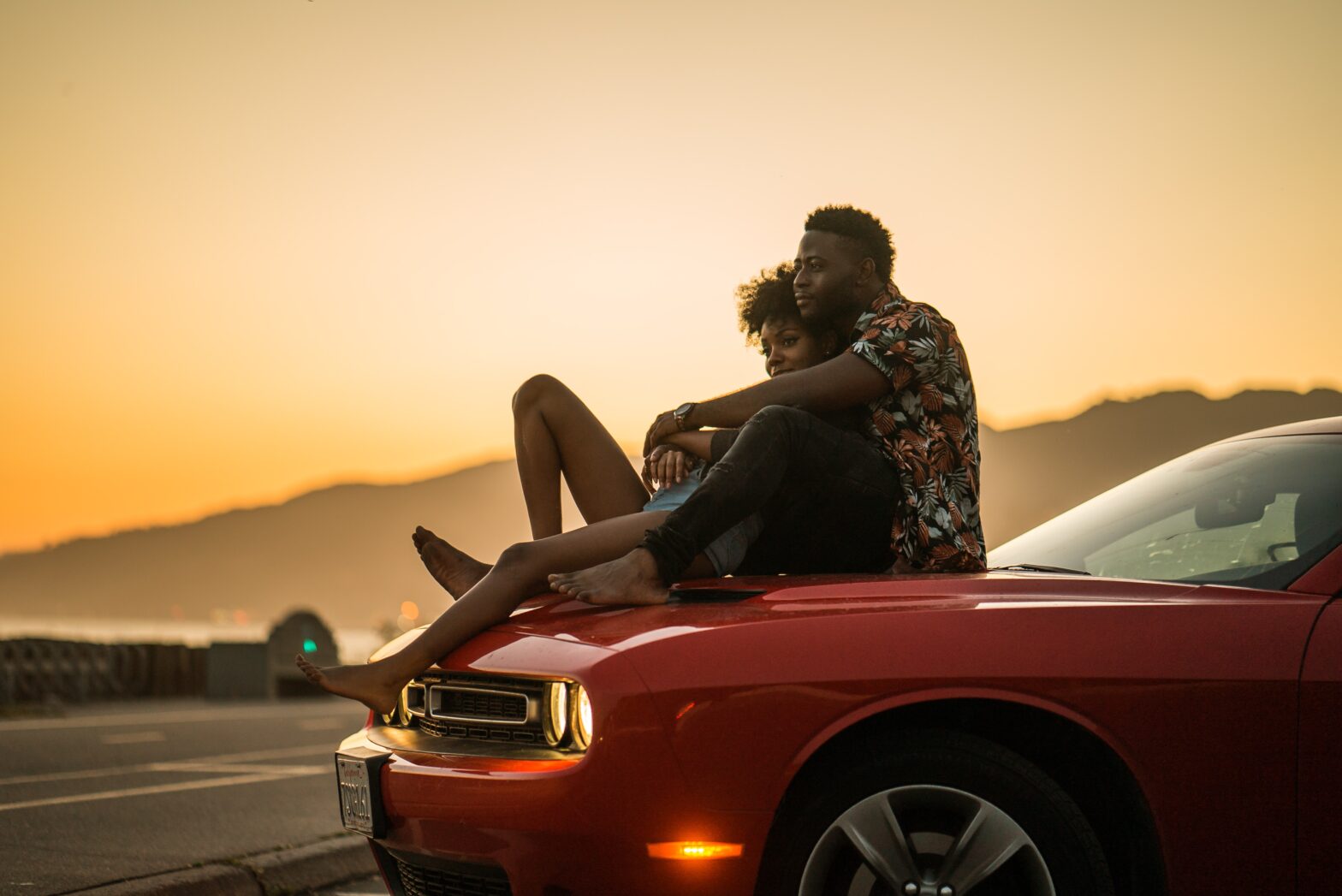 man and woman sitting on the hood of a car