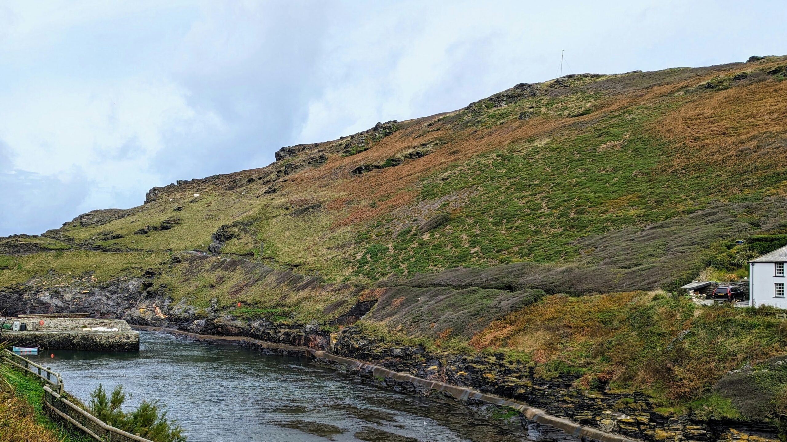 The Sea Cove Cottage is one of the filming locations of the series “Doc Martin”. 
Pictured: a lush green hill with a cottage nearby in Cornwall