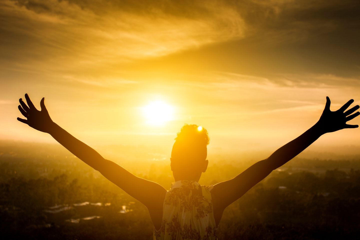 Silhouette of woman stretching arms while overlooking a valley