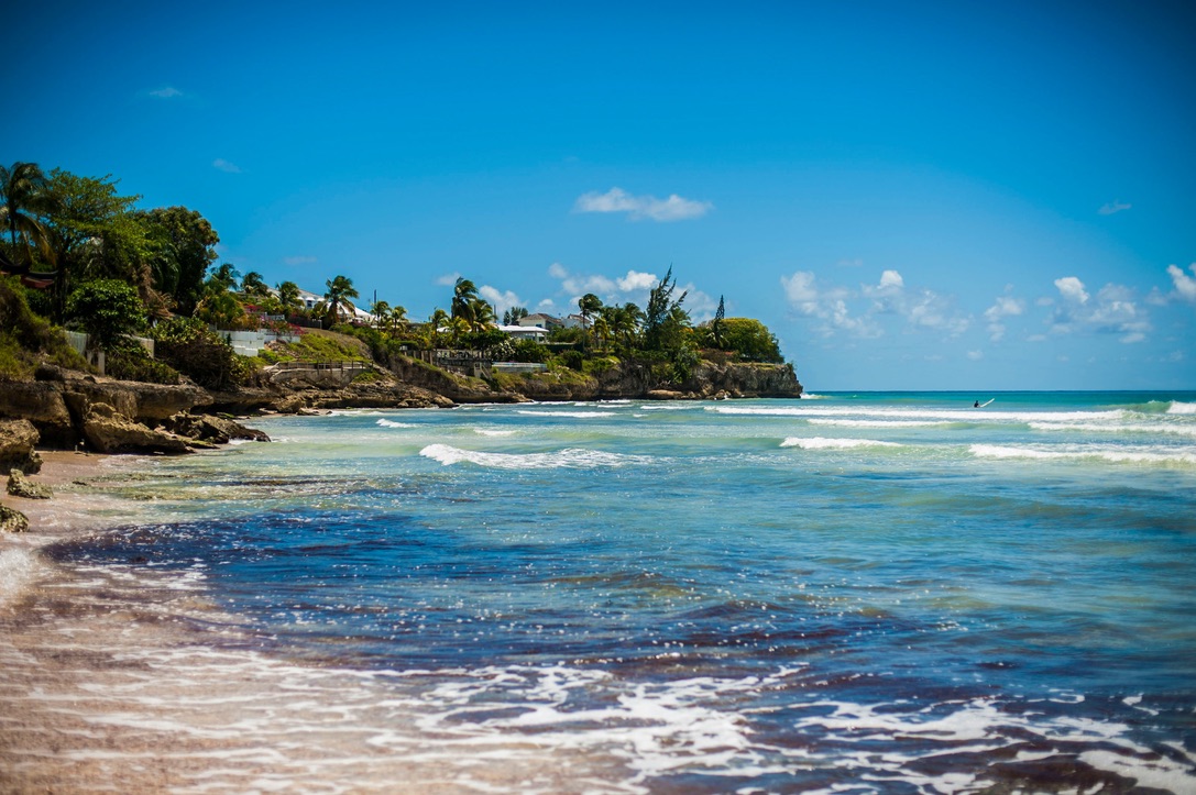 Learn more about why Rihanna's home island is one of her favorite places. pictured: a beach in Barbados with turquoise waters and sunny clear skies