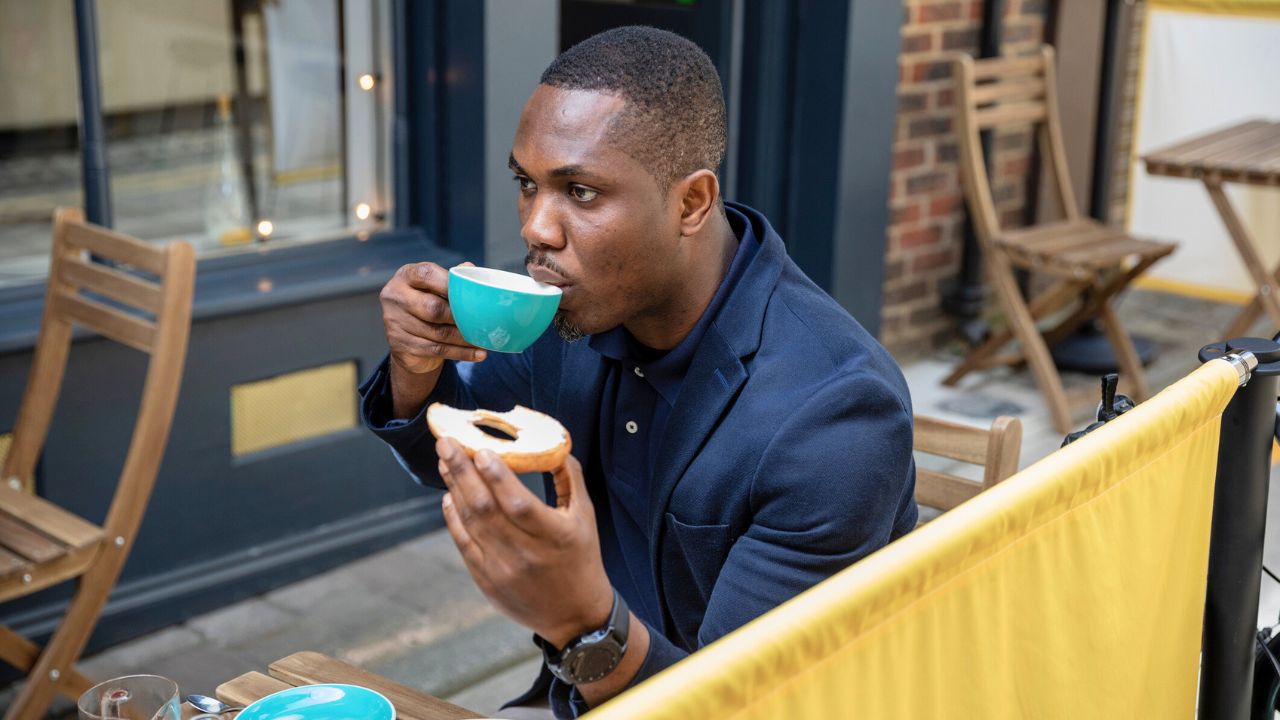 man enjoying a coffee and bagel at an outdoor cafe in a city