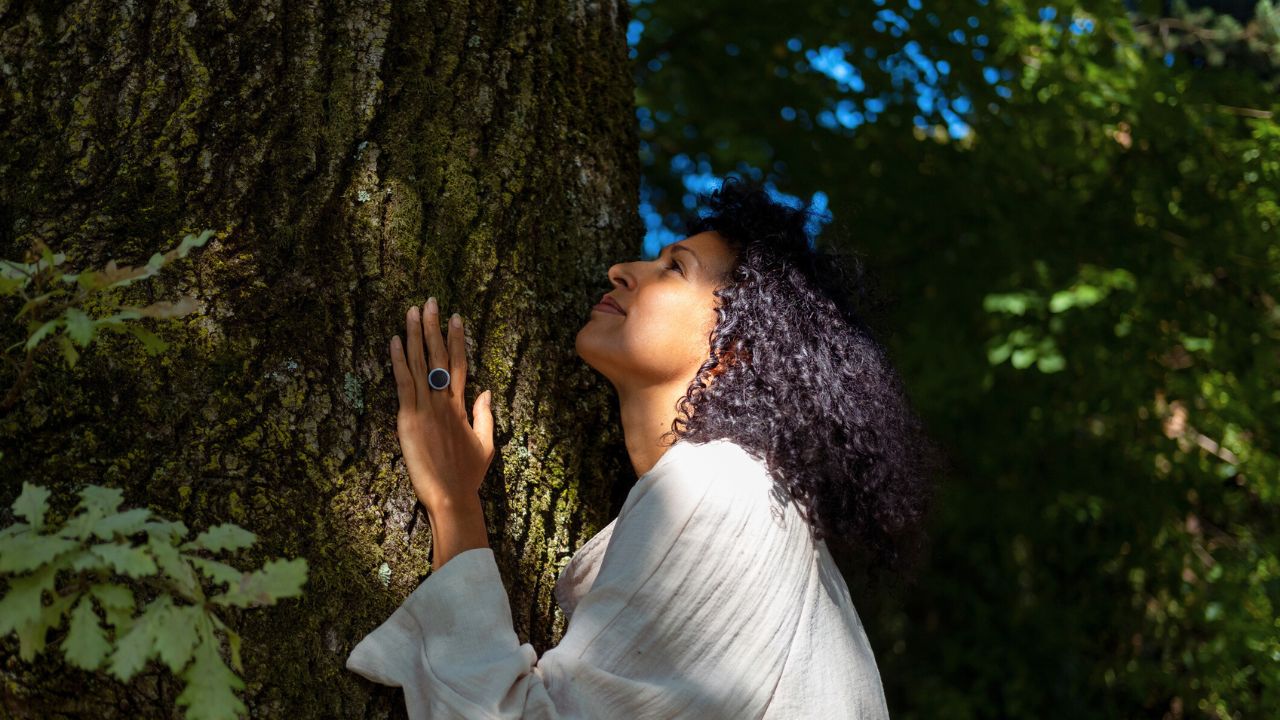 woman calm while connecting with nature by touching a large tree