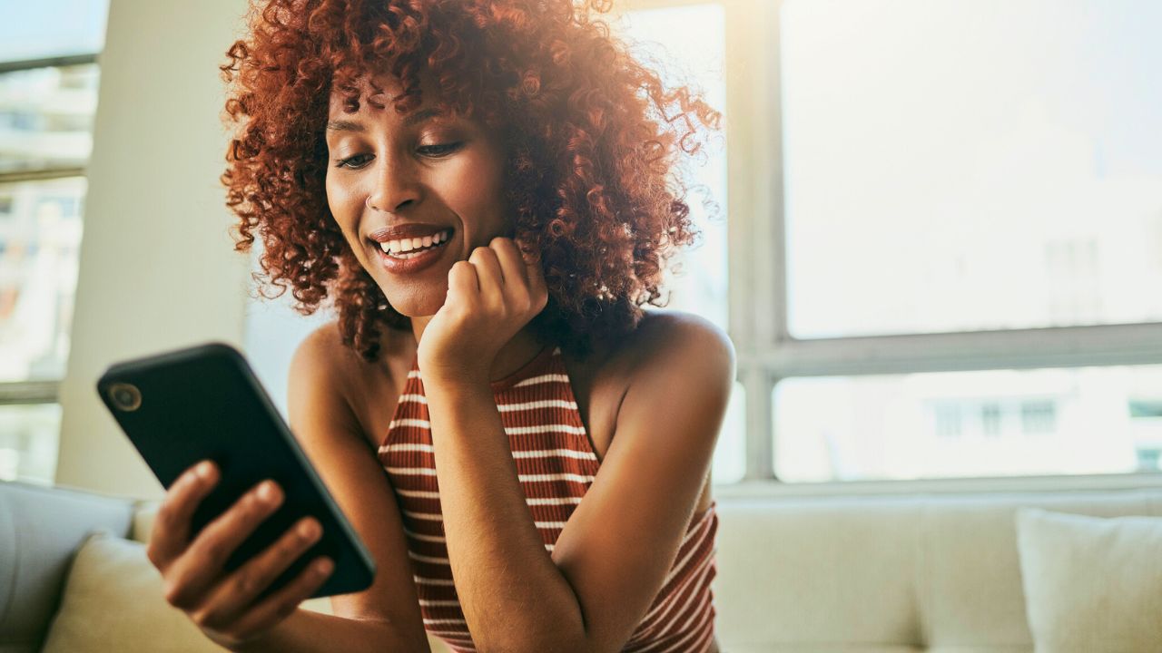 woman smiling while sitting on couch using smartphone