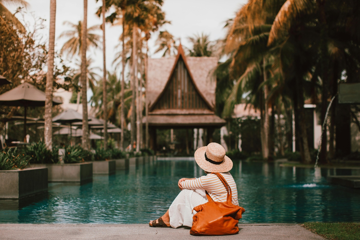 Woman in hat with bag resting near turquoise pond