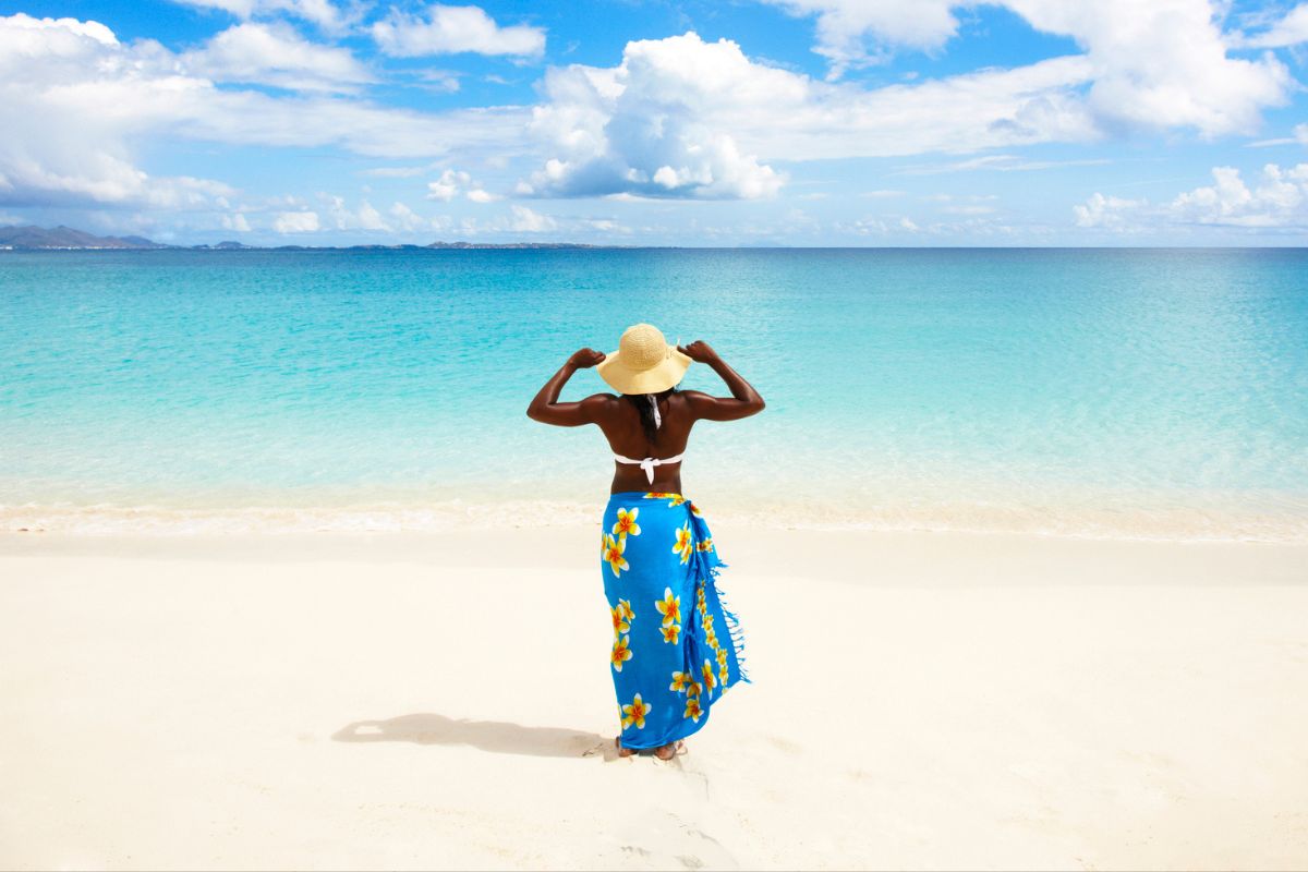 woman in bathing suit with cover up walking toward the ocean on a bright sunny day