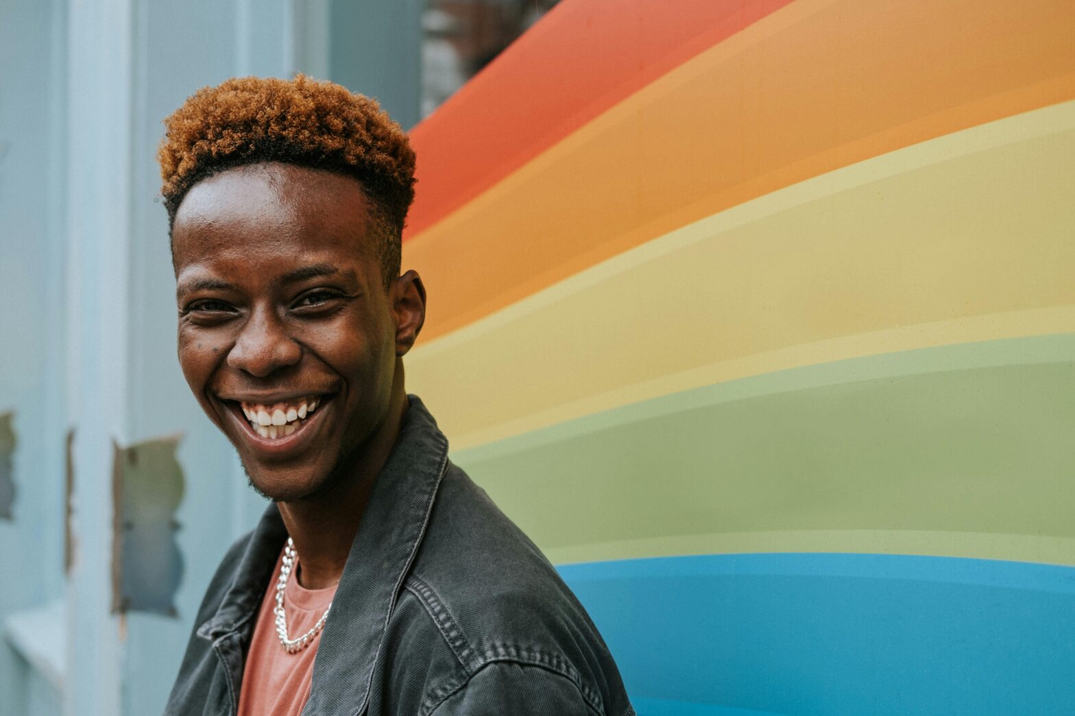 Black person smiling in front of a rainbow wall.