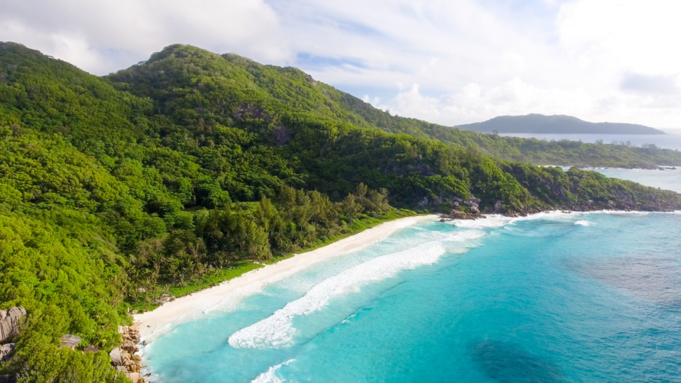 One of Seychelles secret beaches, featuring clear blue ocean water lapping against green hills. 