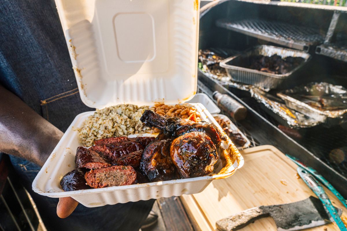 BBQ Chef holding open a Takeout Container with Smoked BBQ Beans, Sausage, Chicken Thighs & Drumsticks, and Dirty Rice from a Food Truck