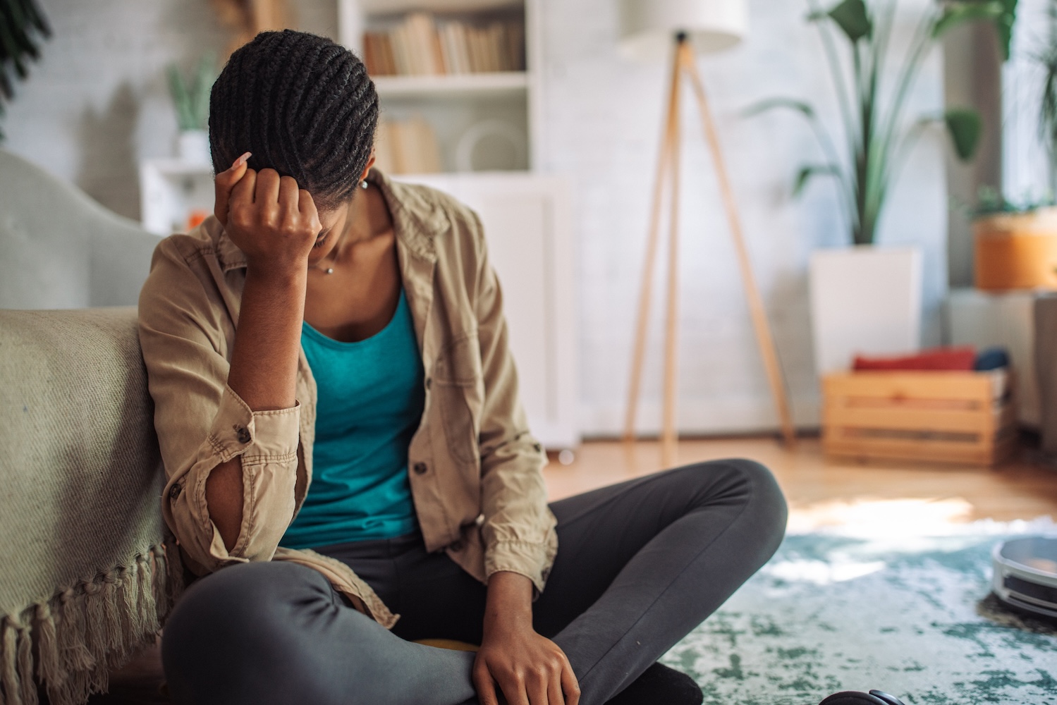 A depressed, stressed woman is sitting on the floor and holding her hand on her head.