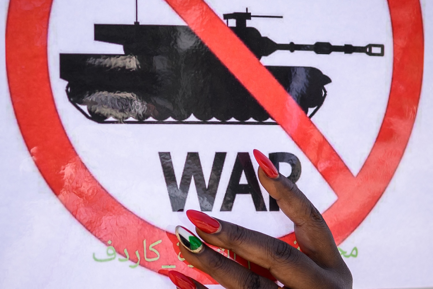 A woman with one of her painted nail adorned with a Sudanese flag holds a placard during a demonstration.