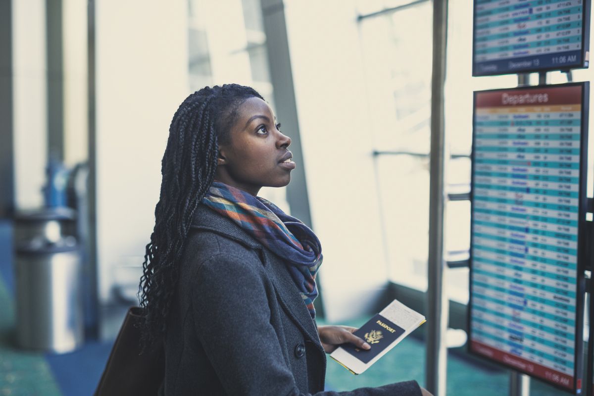 woman looking at flight boards at the airport while holding passport